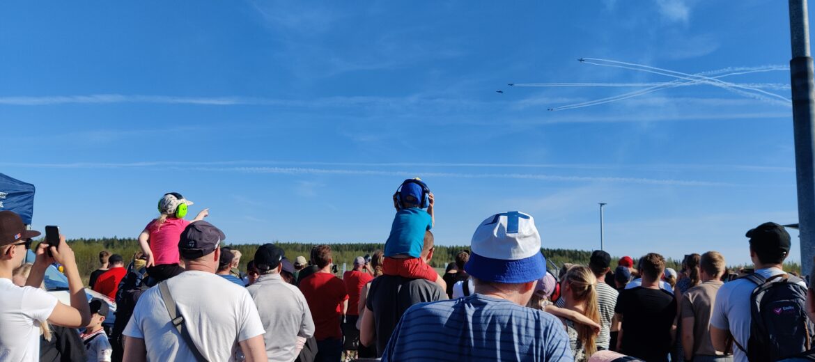 Yleisö katsoo ohi lentäviä lentokoneita lentonäytöksessä. Lapset istuvat aikuisten olkapäillä.