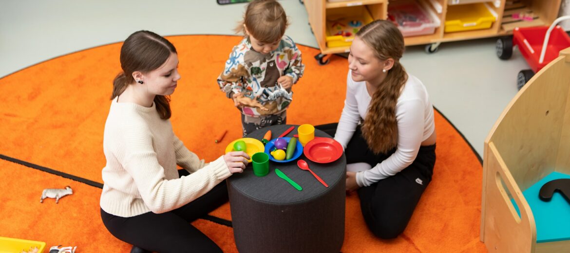 Kaksi Tredun opiskelijaa leikkii taaperon kanssa värikkäässä ympäristössä.